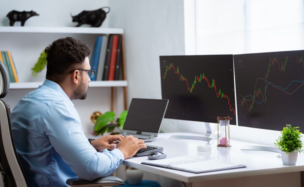 Person working at a desk with dual monitors showing financial charts and analytics.